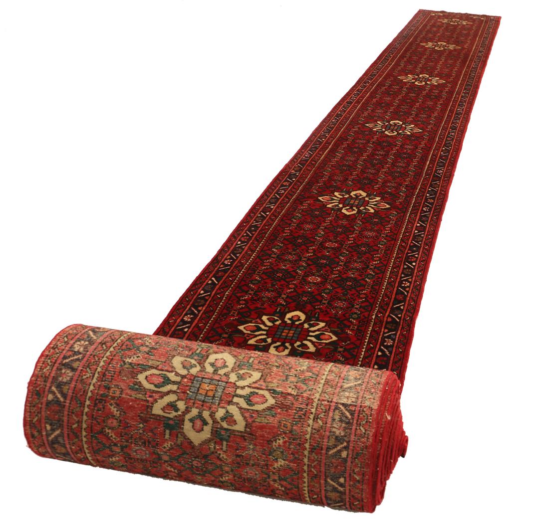 Un long tapis couloir Hosseinabad noué à la main, provenant du Moyen-Orient, arborant un fond rouge vibrant et des motifs floraux détaillés.