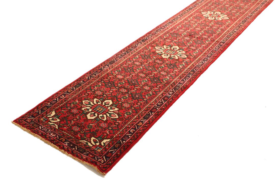 Un long tapis couloir Hosseinabad noué à la main, provenant du Moyen-Orient, arborant un fond rouge vibrant et des motifs floraux détaillés.