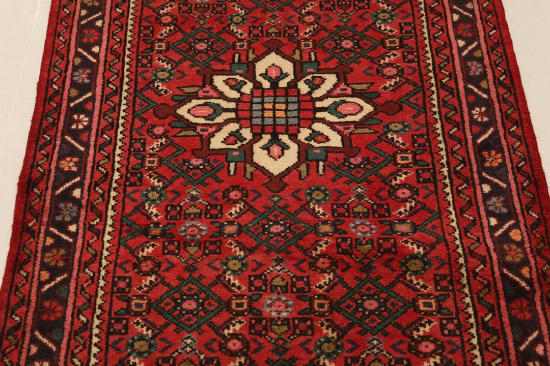 Un long tapis couloir Hosseinabad noué à la main, provenant du Moyen-Orient, arborant un fond rouge vibrant et des motifs floraux détaillés.