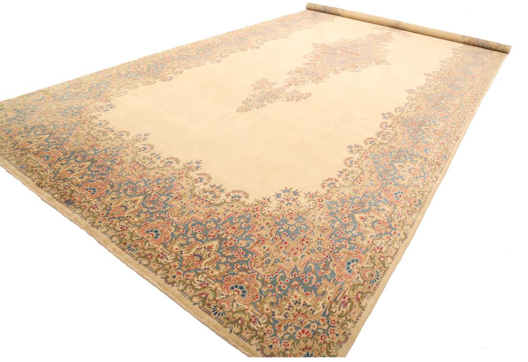 Large Kerman rug from the Middle East featuring a central floral medallion in beige, blue, and pink tones.