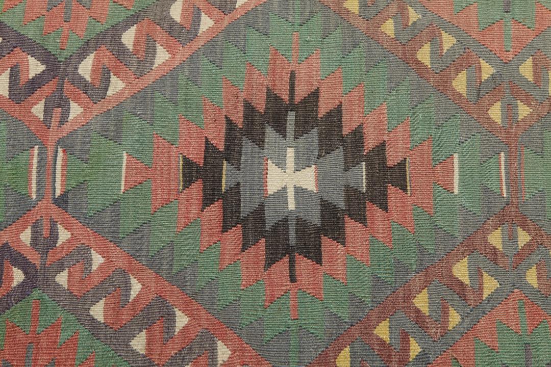 Een vintage Turks Kelim-tapijt met een geometrisch patroon in groene, bruine en rode tinten.