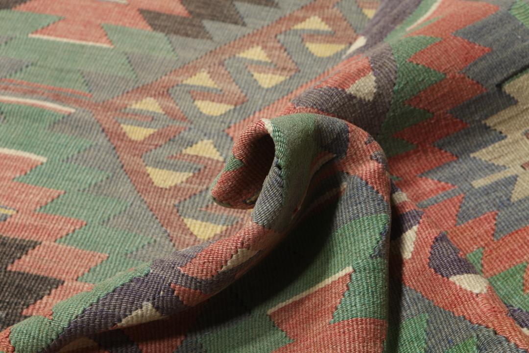 Een vintage Turks Kelim-tapijt met een geometrisch patroon in groene, bruine en rode tinten.