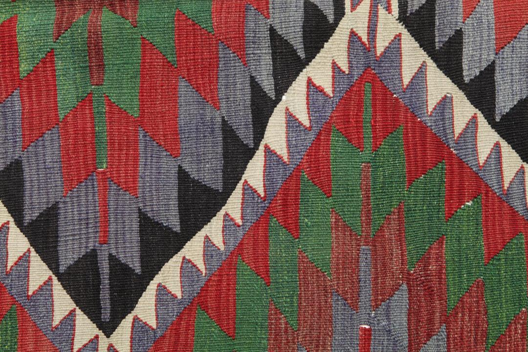 Un tapis Kelim turc vintage tissé à la main présentant un motif géométrique en losange aux couleurs vives rouge, vert et gris foncé.