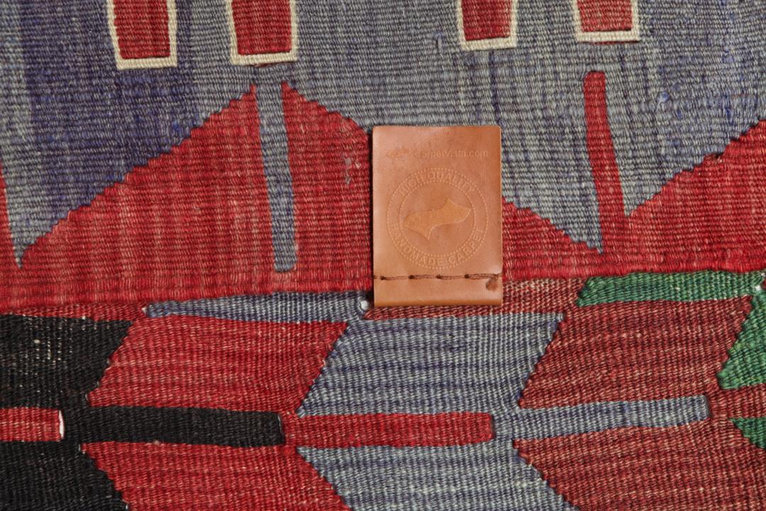 Un tapis Kelim turc vintage tissé à la main présentant un motif géométrique en losange aux couleurs vives rouge, vert et gris foncé.