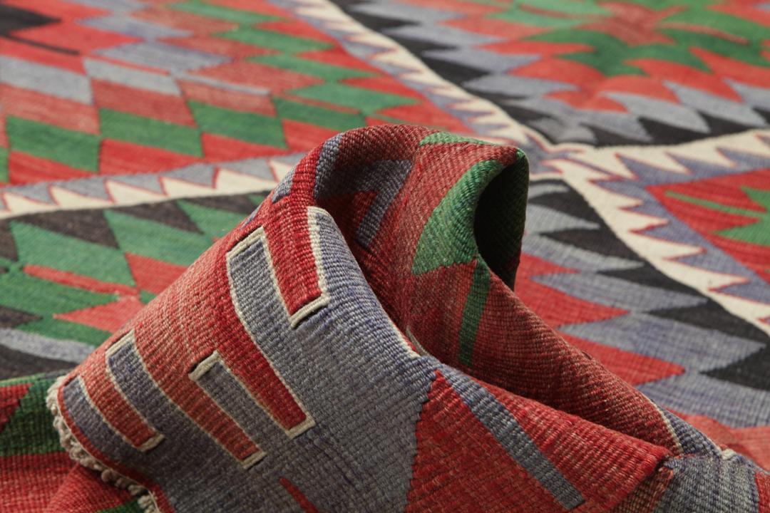 Un tapis Kelim turc vintage tissé à la main présentant un motif géométrique en losange aux couleurs vives rouge, vert et gris foncé.