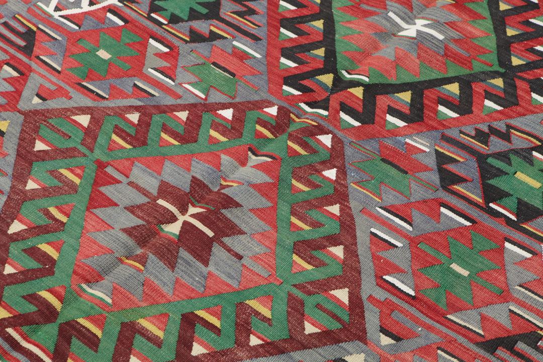 Tapis Kilim vintage tissé à la main originaire de Turquie avec des motifs géométriques colorés en rouge, vert et gris.