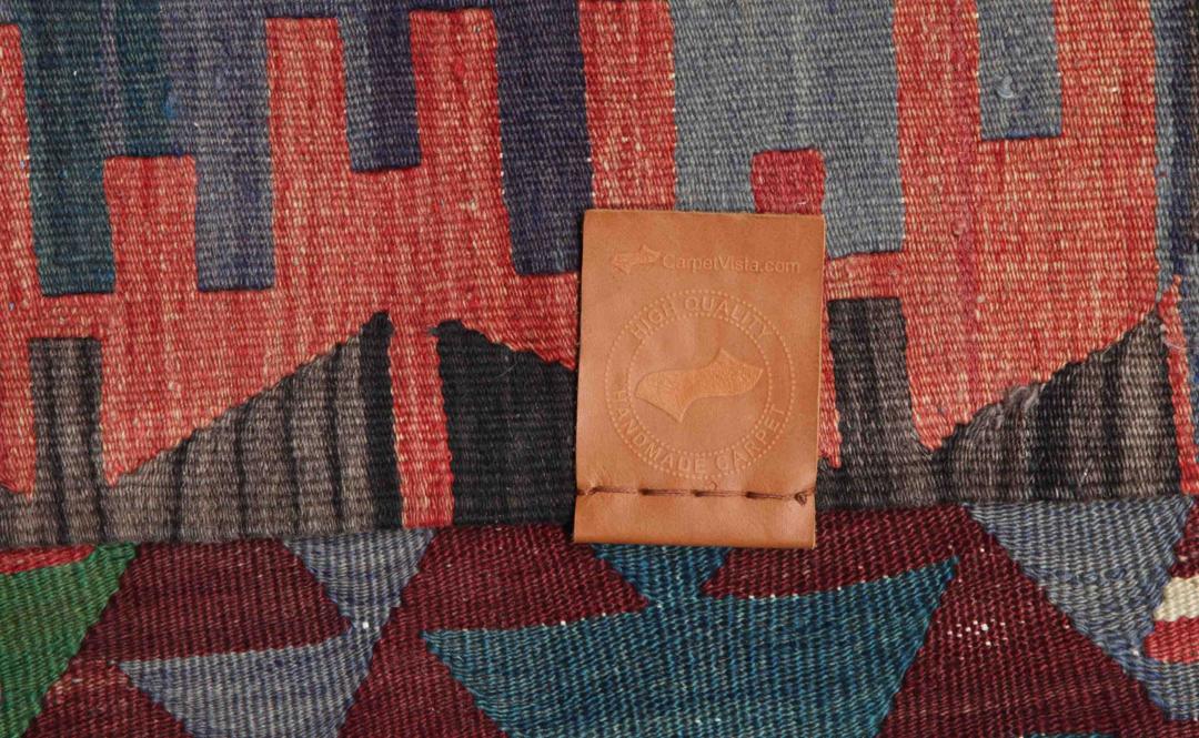 Tapis Kilim vintage tissé à la main originaire de Turquie avec des motifs géométriques colorés en rouge, vert et gris.