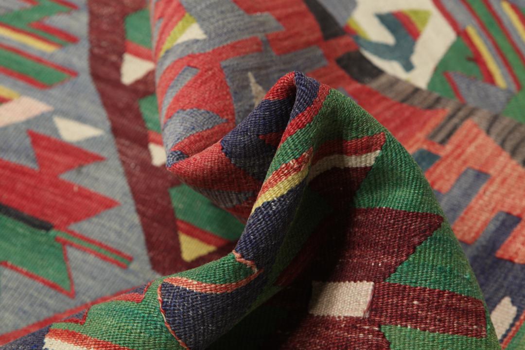 Tapis Kilim vintage tissé à la main originaire de Turquie avec des motifs géométriques colorés en rouge, vert et gris.