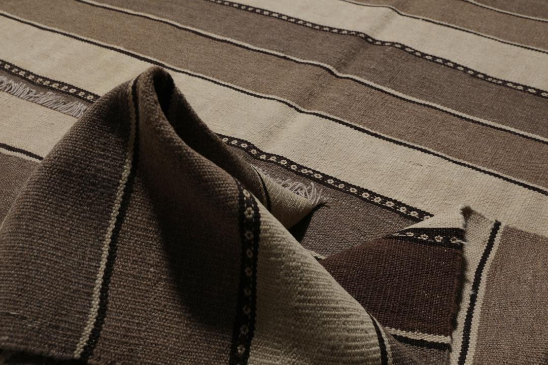 Et håndvævet kelimtæppe fra Mellemøsten med vandrette brune og beige striber.
