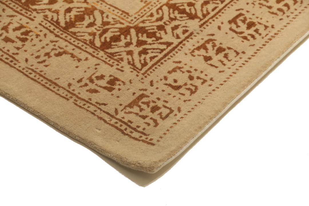 Et stort rektangulært indisk tæppe med en beige flade og indviklede gyldne mønstre.
