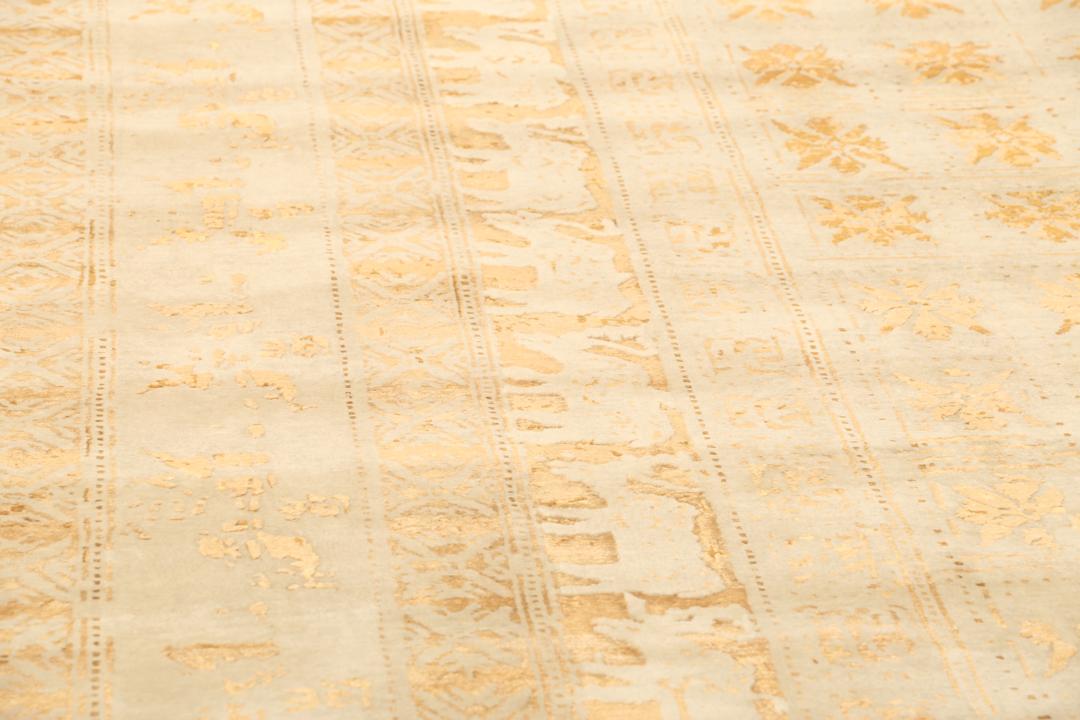 Et stort rektangulært indisk tæppe med en beige flade og indviklede gyldne mønstre.