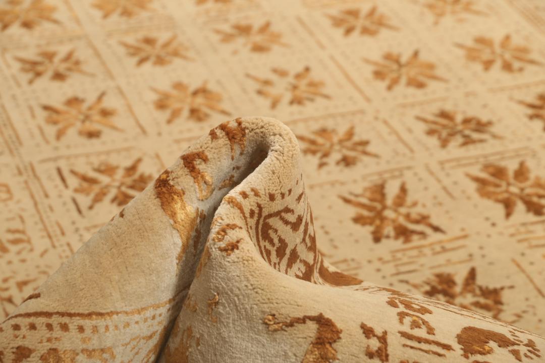 Et stort rektangulært indisk tæppe med en beige flade og indviklede gyldne mønstre.