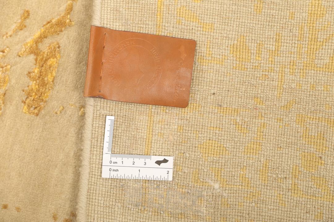 Et luksuriøst håndknyttet tæppe fra Indien med et skinnende gyldent mønster på en beige bund
