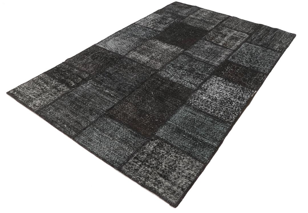 Een rechthoekig handgemaakt patchwork vloerkleed uit Turkije in zwarte en donkergrijze tinten.