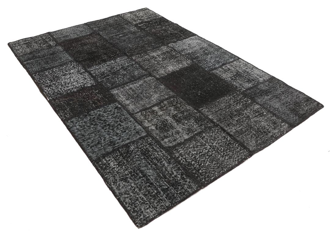 Een rechthoekig handgemaakt patchwork vloerkleed uit Turkije in zwarte en donkergrijze tinten.