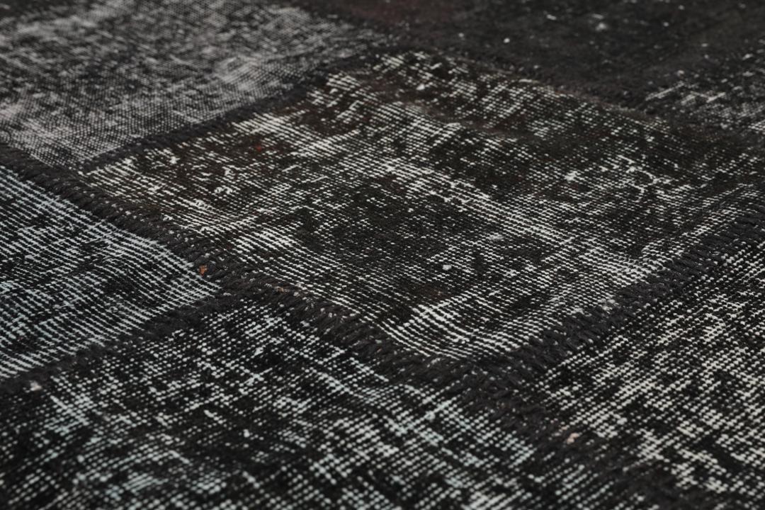 Een rechthoekig handgemaakt patchwork vloerkleed uit Turkije in zwarte en donkergrijze tinten.
