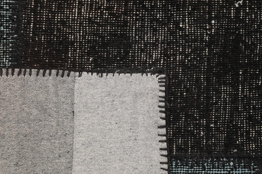 Een rechthoekig handgemaakt patchwork vloerkleed uit Turkije in zwarte en donkergrijze tinten.
