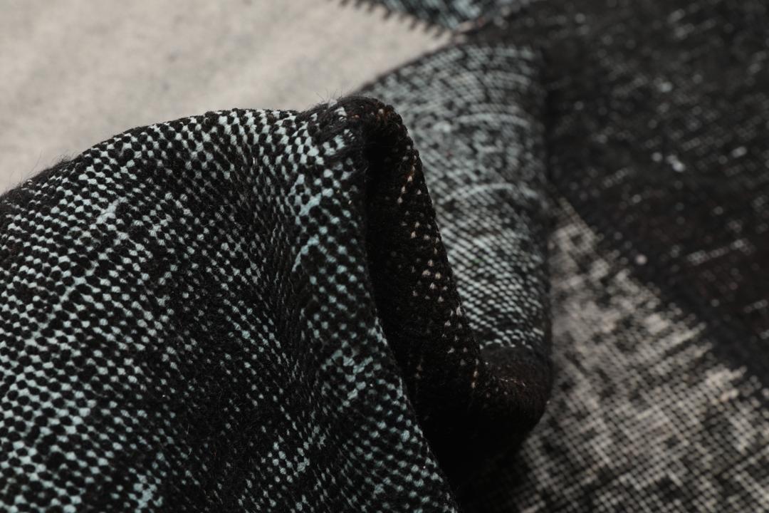 Een rechthoekig handgemaakt patchwork vloerkleed uit Turkije in zwarte en donkergrijze tinten.
