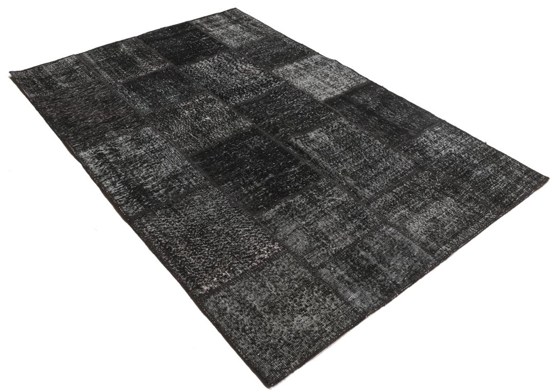 Een zwart patchwork vloerkleed handgemaakt in Turkije met gevarieerde texturen en tinten.