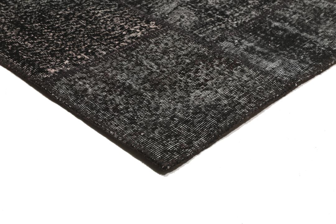 Een zwart patchwork vloerkleed handgemaakt in Turkije met gevarieerde texturen en tinten.