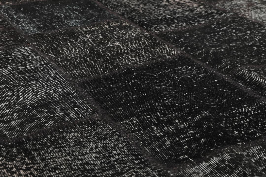 Een zwart patchwork vloerkleed handgemaakt in Turkije met gevarieerde texturen en tinten.