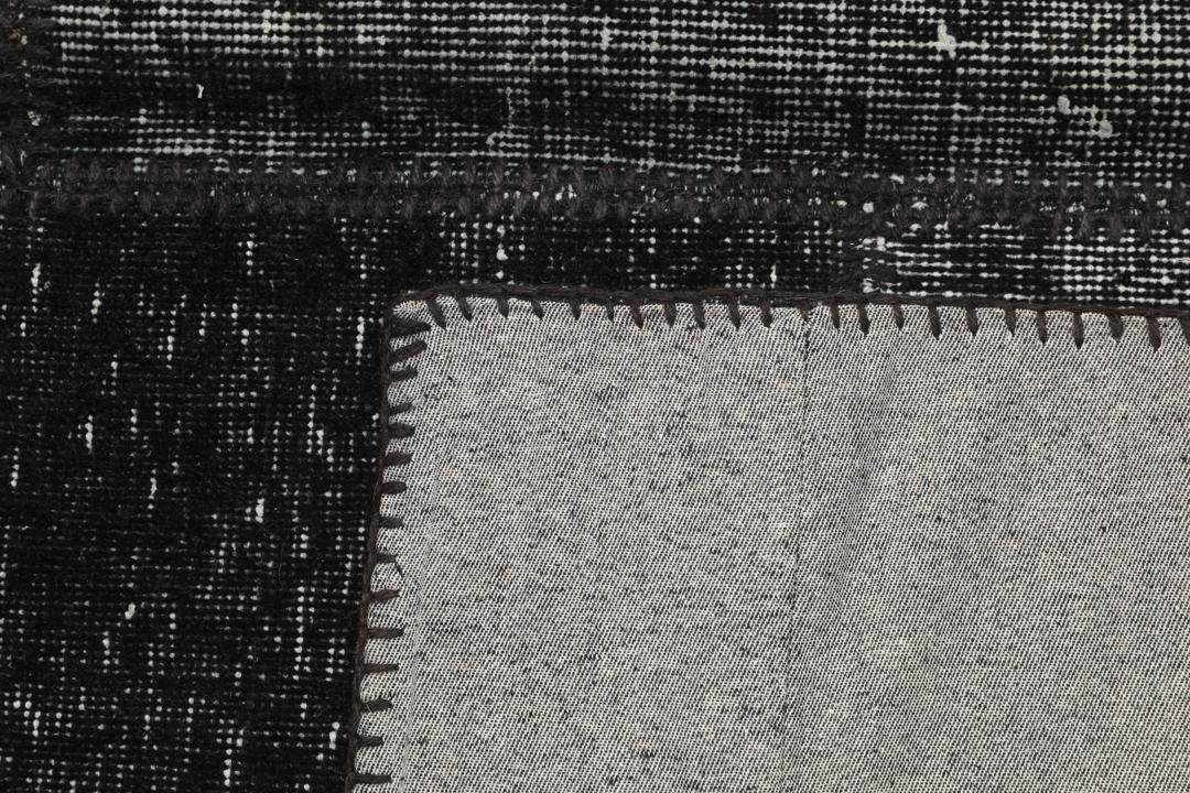 Een zwart patchwork vloerkleed handgemaakt in Turkije met gevarieerde texturen en tinten.