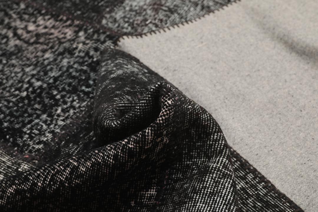 Een zwart patchwork vloerkleed handgemaakt in Turkije met gevarieerde texturen en tinten.