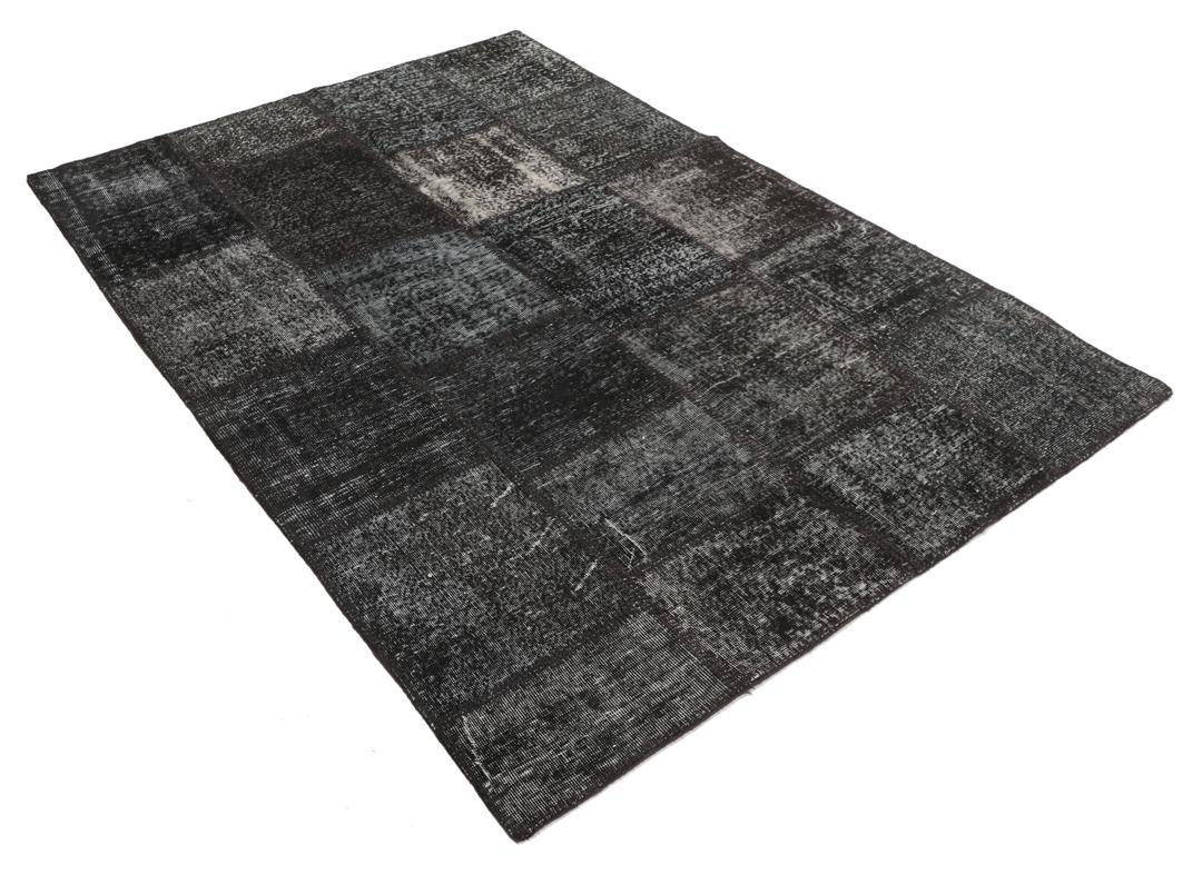 Een zwart patchwork vloerkleed met handgeknoopte wollen fragmenten in verschillende tinten uit Turkije.