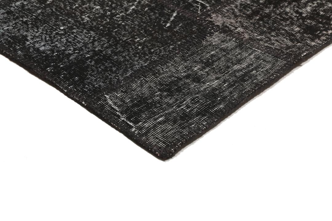 Een zwart patchwork vloerkleed met handgeknoopte wollen fragmenten in verschillende tinten uit Turkije.