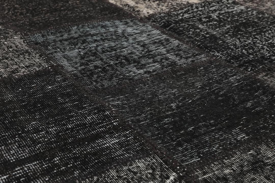 Een zwart patchwork vloerkleed met handgeknoopte wollen fragmenten in verschillende tinten uit Turkije.