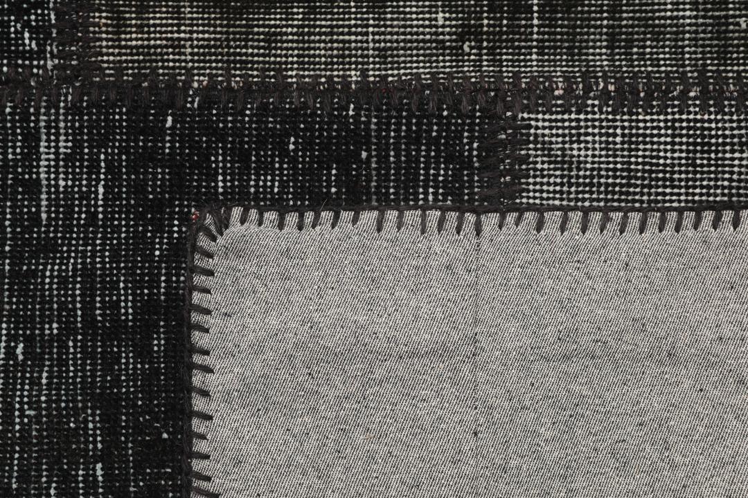 Een zwart patchwork vloerkleed met handgeknoopte wollen fragmenten in verschillende tinten uit Turkije.