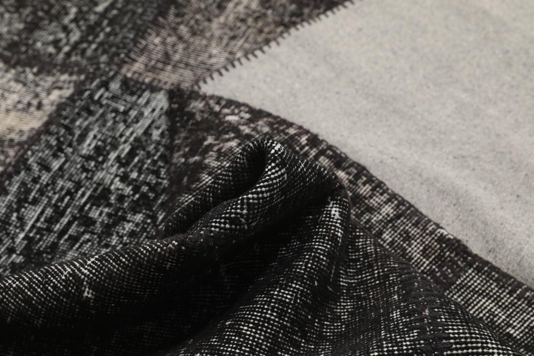 Een zwart patchwork vloerkleed met handgeknoopte wollen fragmenten in verschillende tinten uit Turkije.