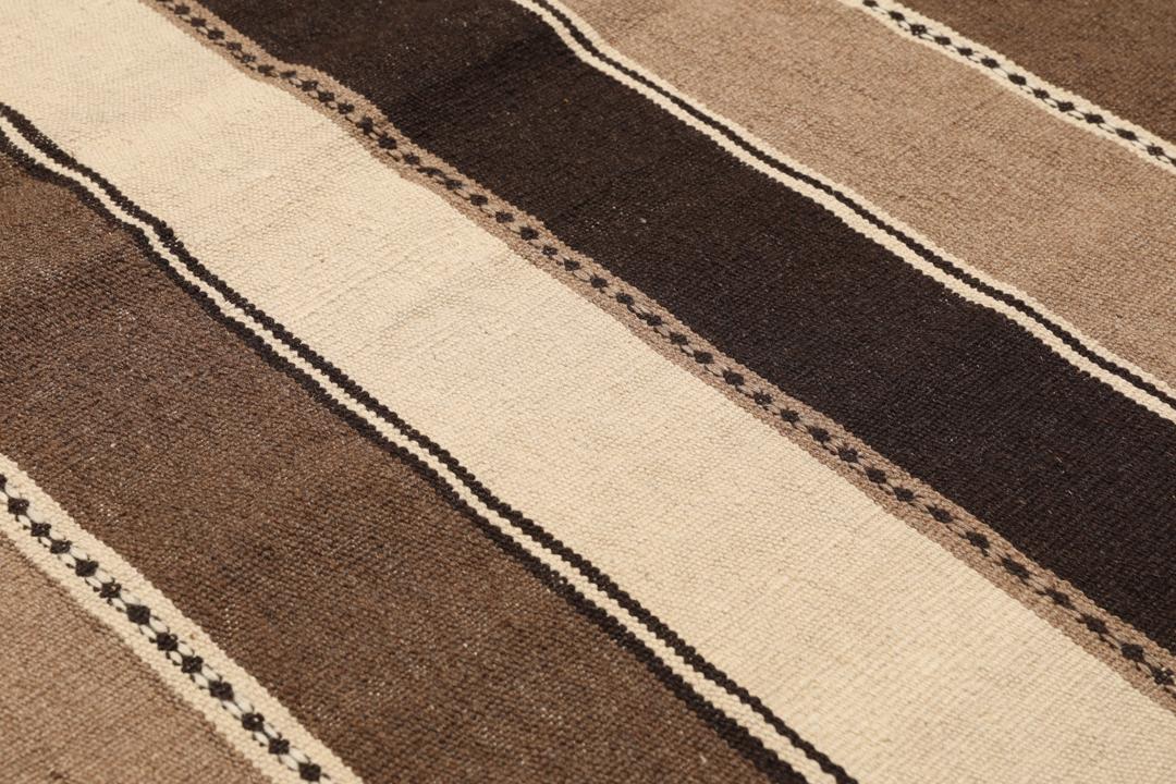 Et håndvævet Kelim-tæppe fra Mellemøsten med vandrette striber i brune, beige og mørke nuancer