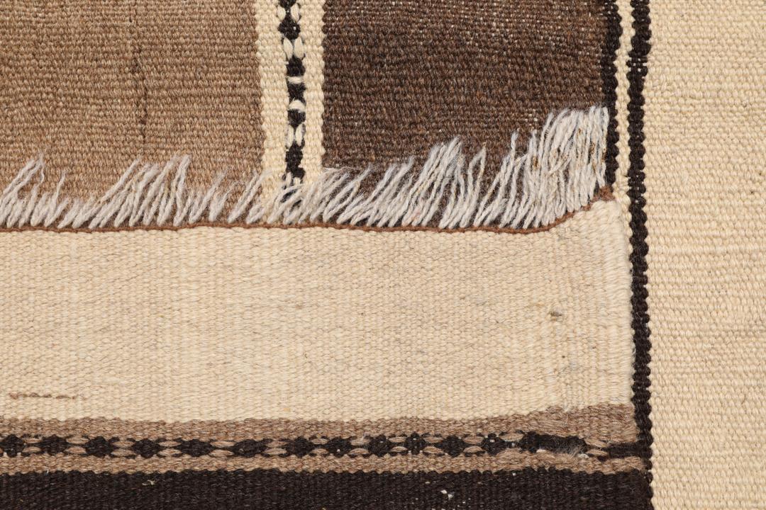 Et håndvævet Kelim-tæppe fra Mellemøsten med vandrette striber i brune, beige og mørke nuancer