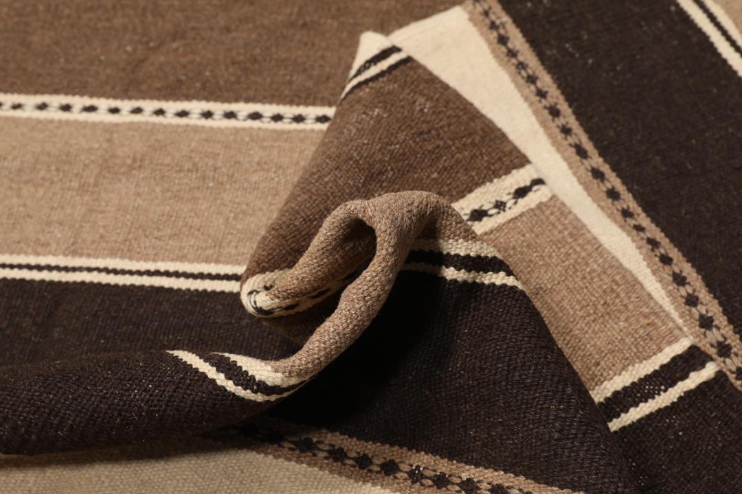 Et håndvævet Kelim-tæppe fra Mellemøsten med vandrette striber i brune, beige og mørke nuancer