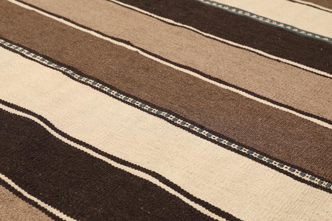 Et håndvævet brunt og beige stribet Kelim-tæppe fra Mellemøsten.
