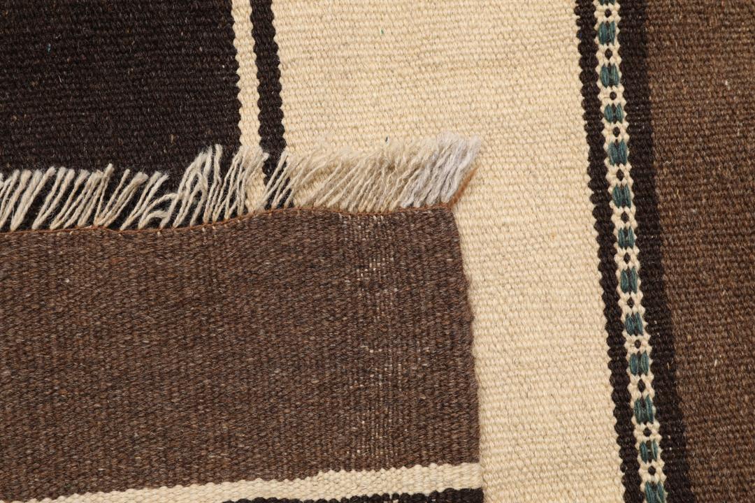 Et håndvævet brunt og beige stribet Kelim-tæppe fra Mellemøsten.