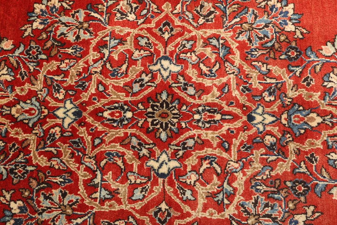 A hand-knotted Sarough rug from the Middle East featuring a red field and intricate floral medallion.