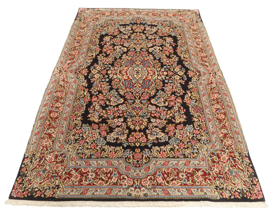 Een handgeknoopt Kerman-tapijt uit het Midden-Oosten met een diepblauw veld en bloemmotieven