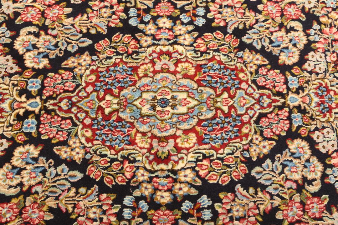 Een handgeknoopt Kerman-tapijt uit het Midden-Oosten met een diepblauw veld en bloemmotieven