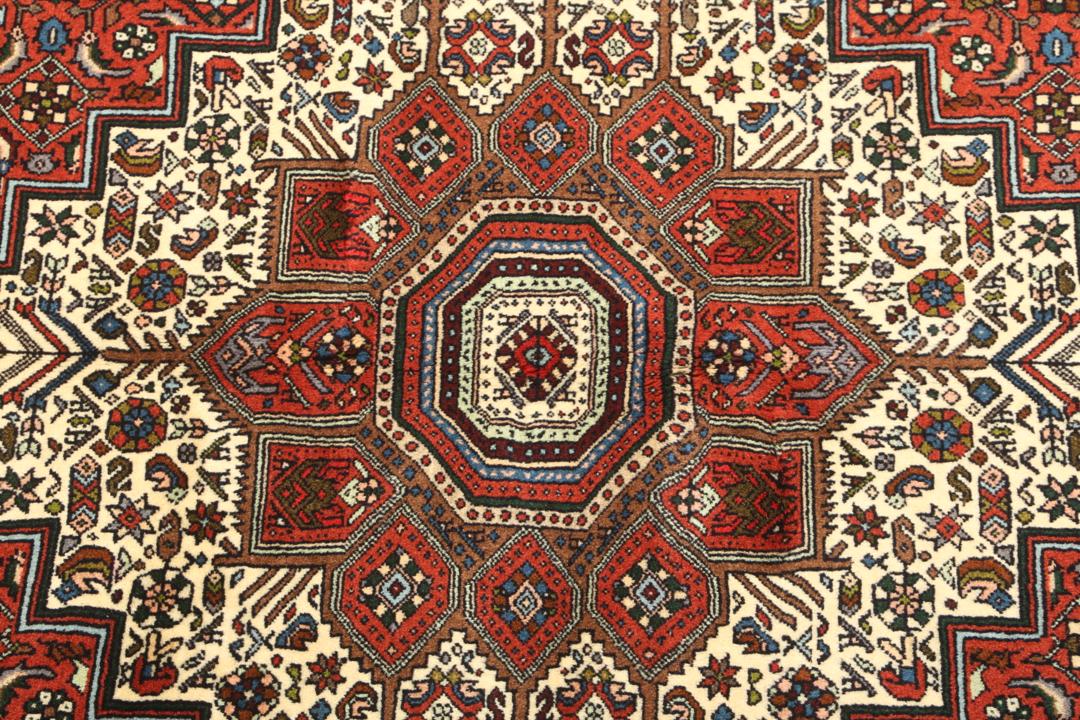 Een handgeknoopt Gholtogh-tapijt uit het Midden-Oosten met een levendig rood en beige medaillonontwerp.