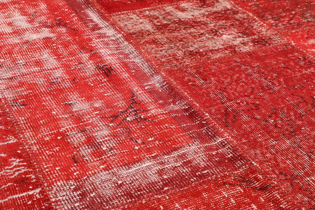 Et rødt patchwork-teppe med varierte håndknyttede fragmenter fra Tyrkia.