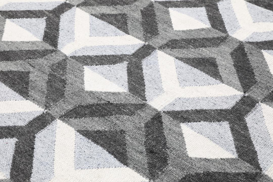 Handgeweven wollen tapijt in grijs en lichtgrijs met een geometrisch patroon.