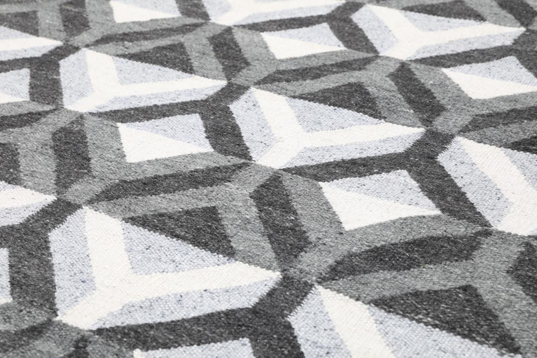 Håndvævet uldtæppe i grå og lysegrå nuancer med et geometrisk mønster.