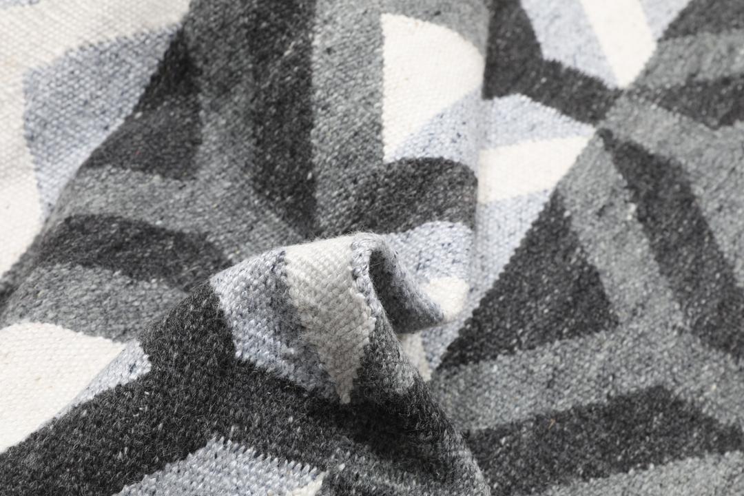 Håndvævet uldtæppe i grå og lysegrå nuancer med et geometrisk mønster.