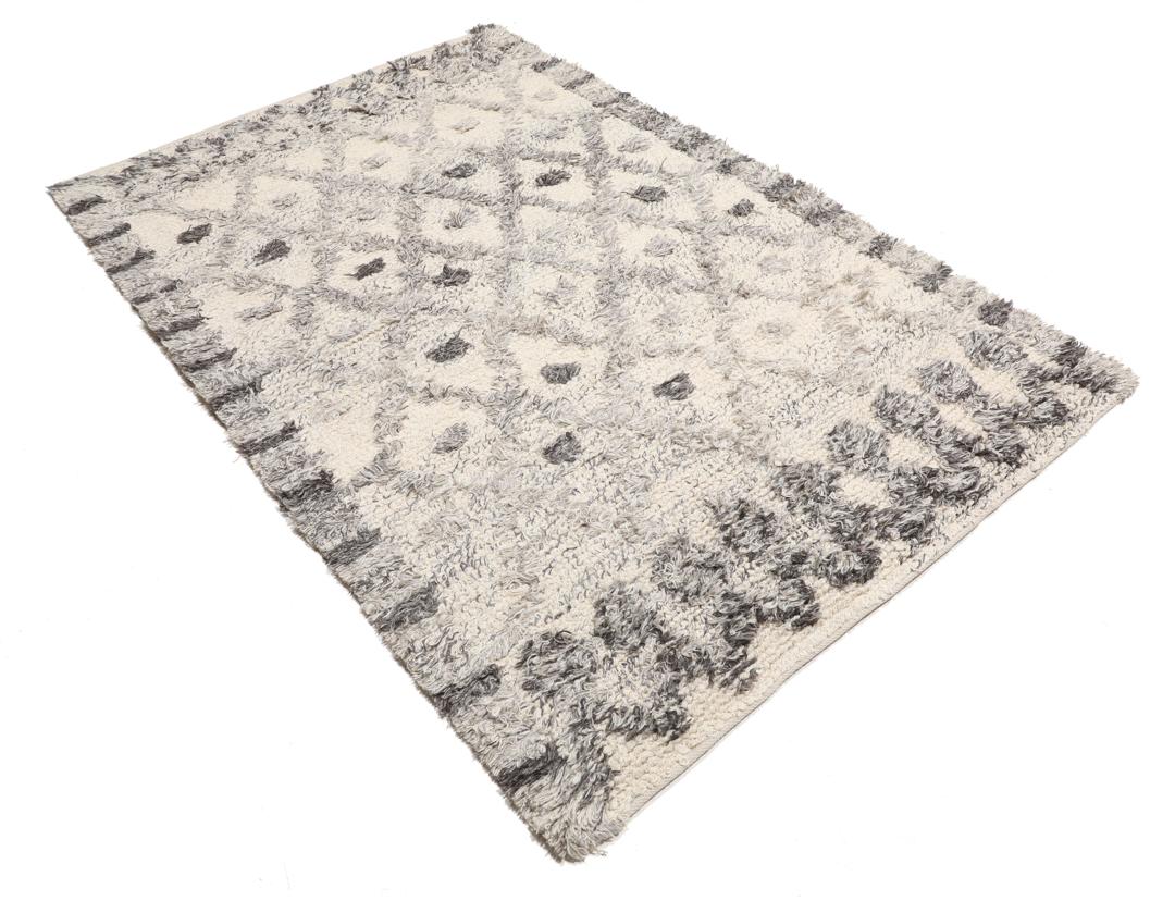 Uma carpete de lã tecida à mão em cinzento e branco creme com um padrão geométrico de diamante.