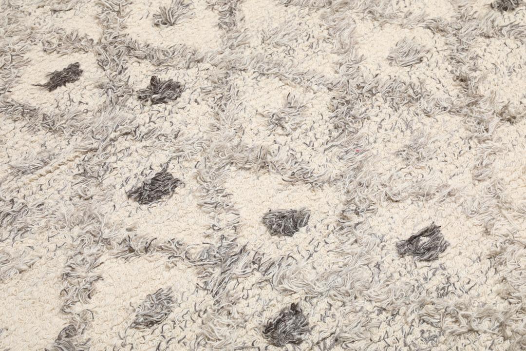 Uma carpete de lã tecida à mão em cinzento e branco creme com um padrão geométrico de diamante.