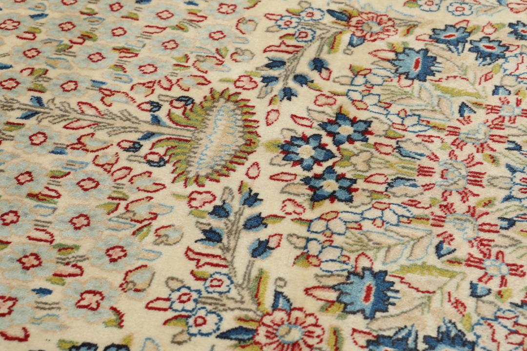 Een handgeknoopt Kerman-tapijt uit het Midden-Oosten met bloempatronen in beige en blauw.