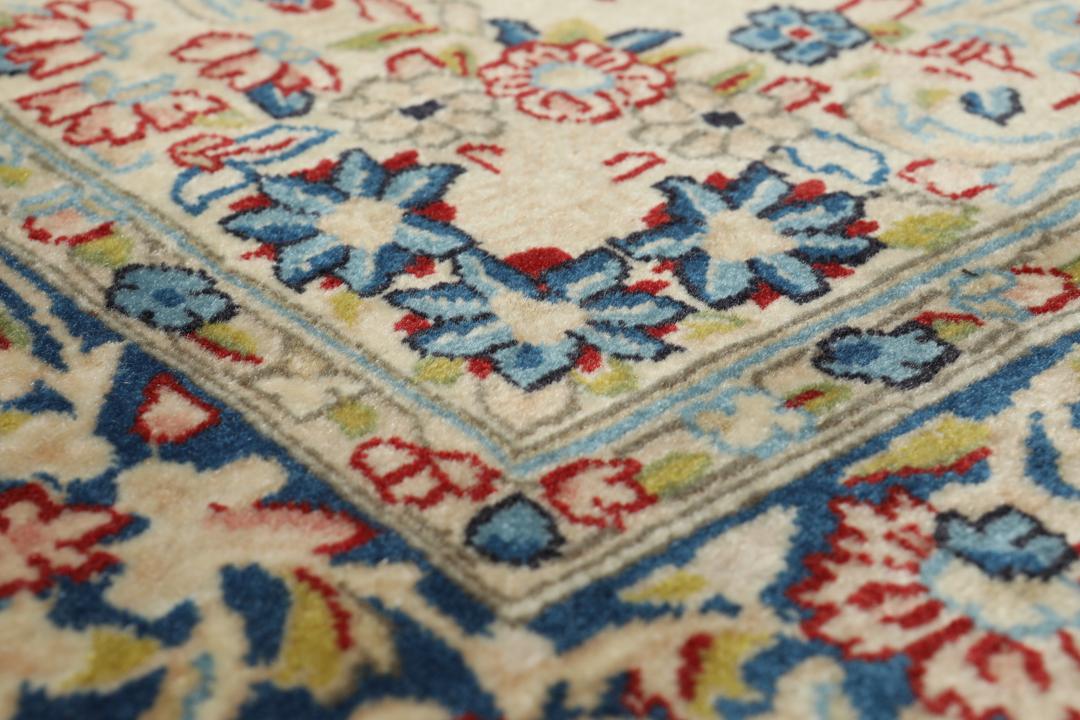 Een handgeknoopt Kerman-tapijt uit het Midden-Oosten met bloempatronen in beige en blauw.