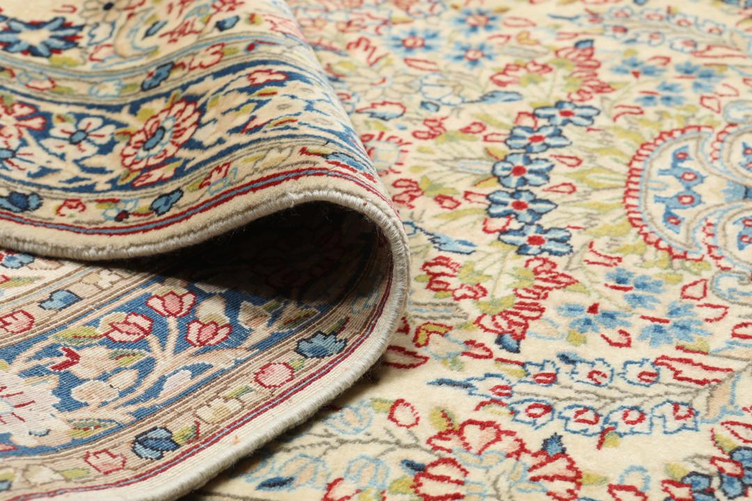 Een handgeknoopt Kerman-tapijt uit het Midden-Oosten met bloempatronen in beige en blauw.